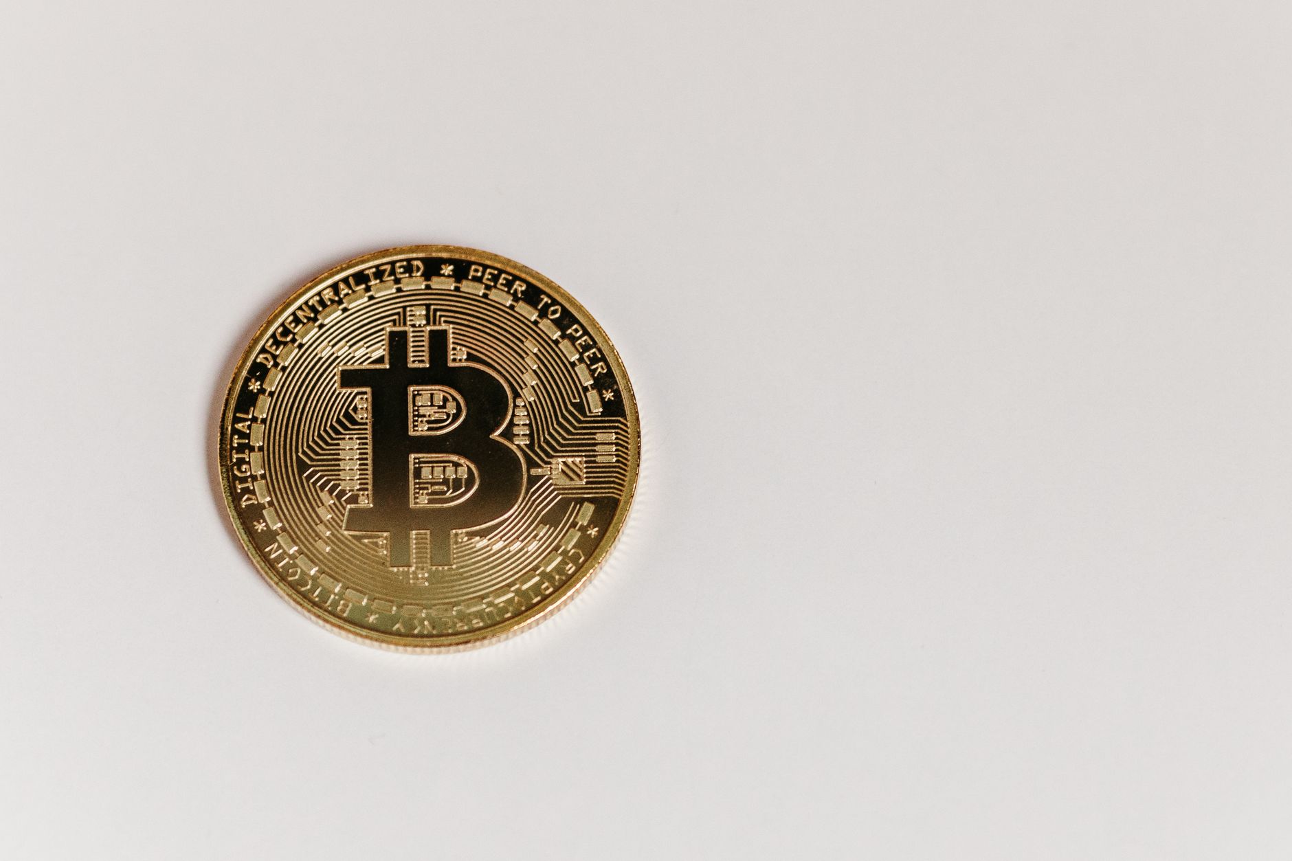 High-quality close-up of a gold Bitcoin coin on a white surface, emphasizing digital currency.