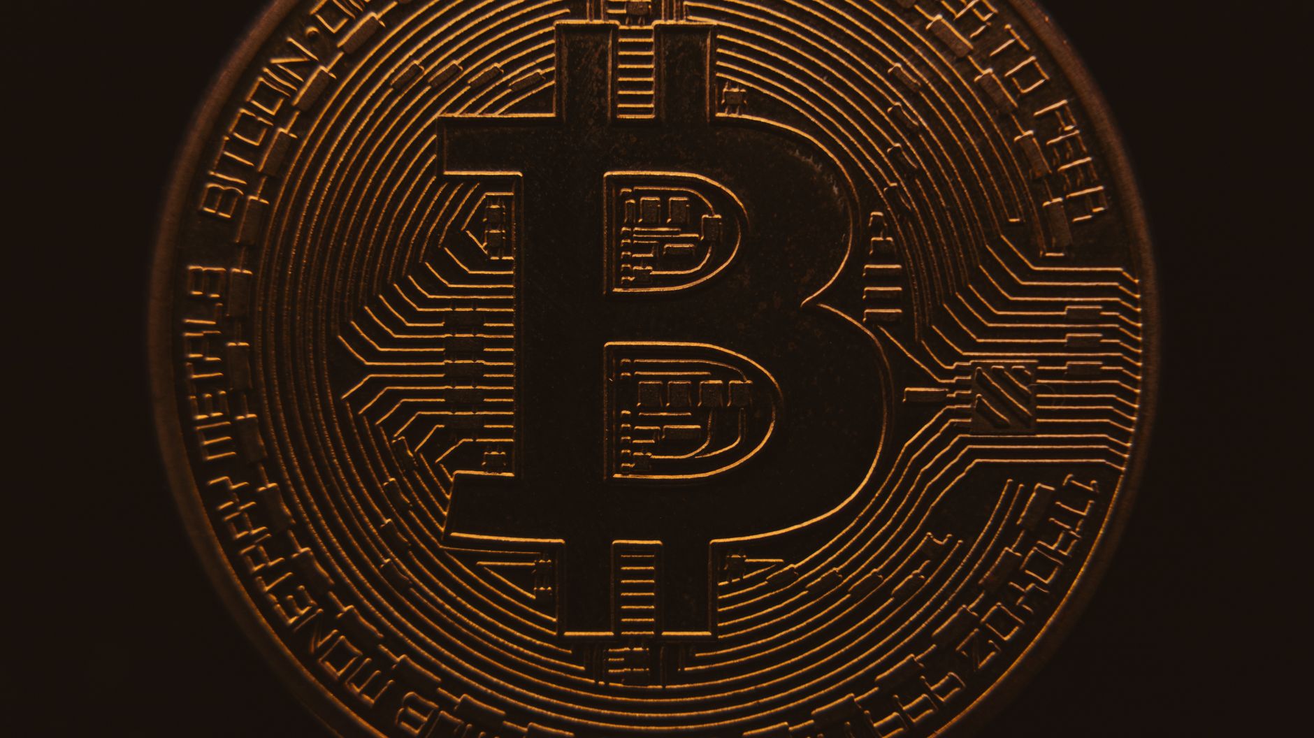 Close-up view of a bitcoin coin showing its intricate, digital design in a warm, dark ambiance.