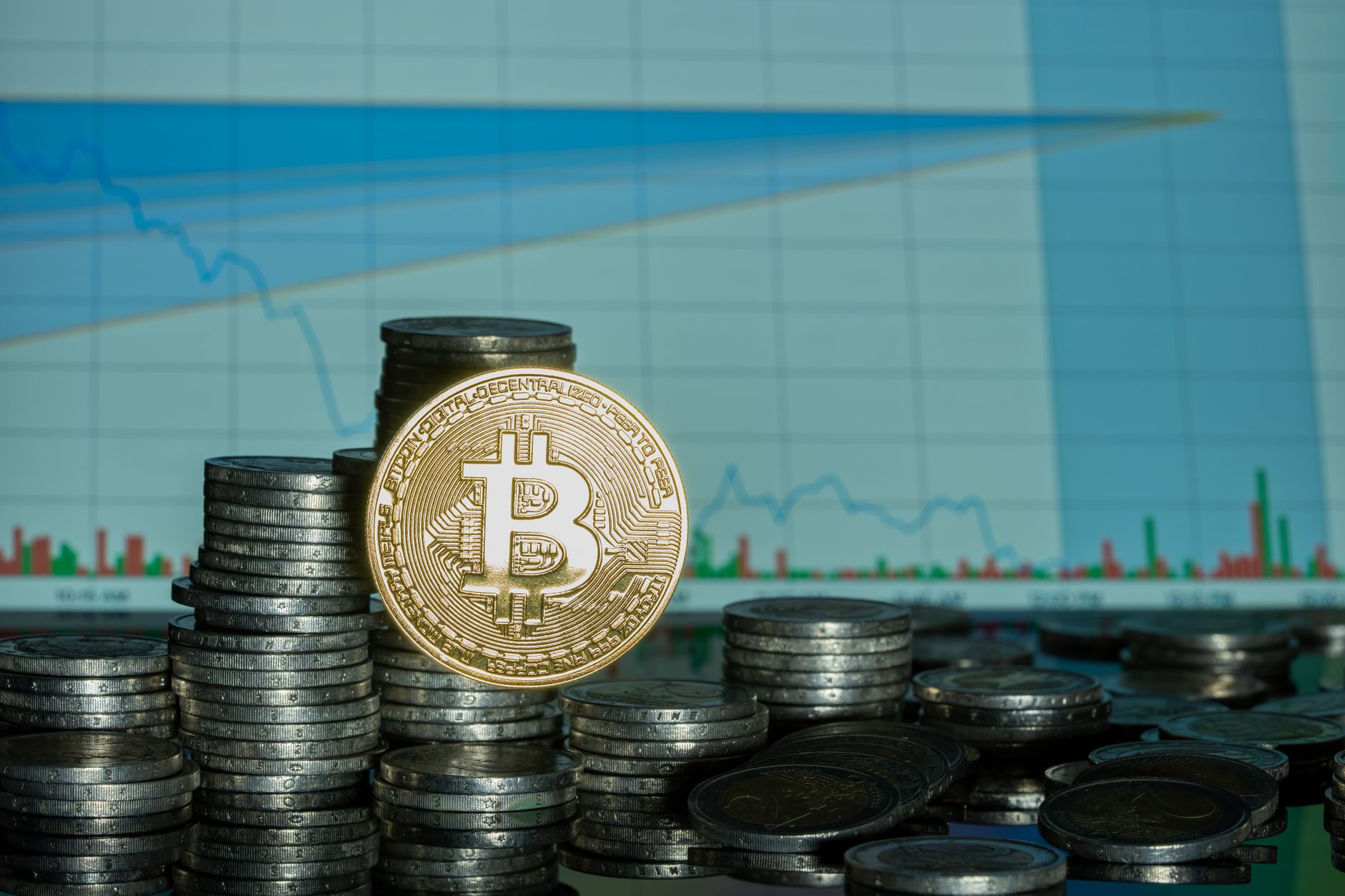 Stack of coins with Bitcoin emblem against a financial market graph, highlighting economic trends.