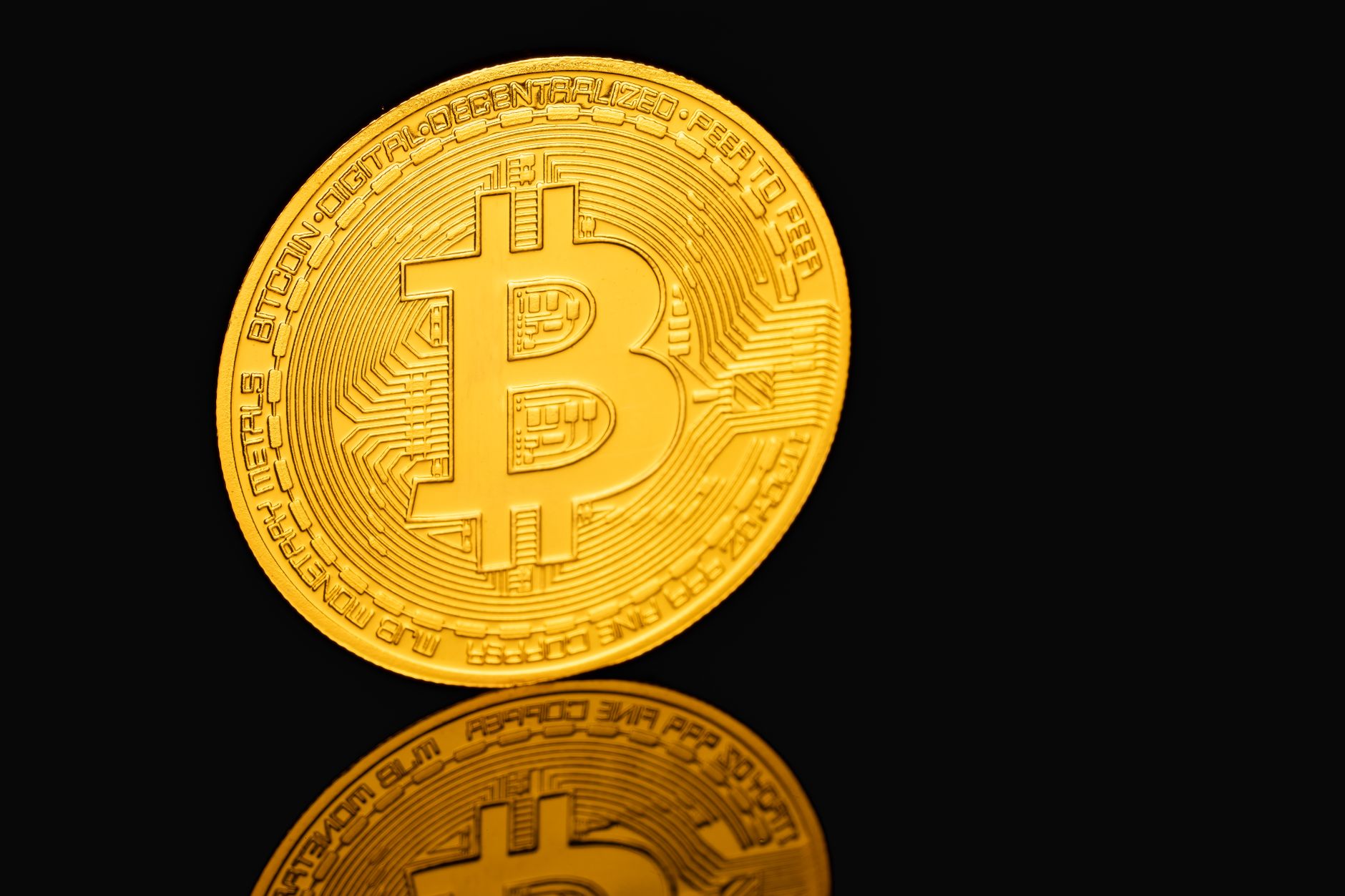 Close-up of a gold Bitcoin coin reflecting on a black surface, symbolizing cryptocurrency.