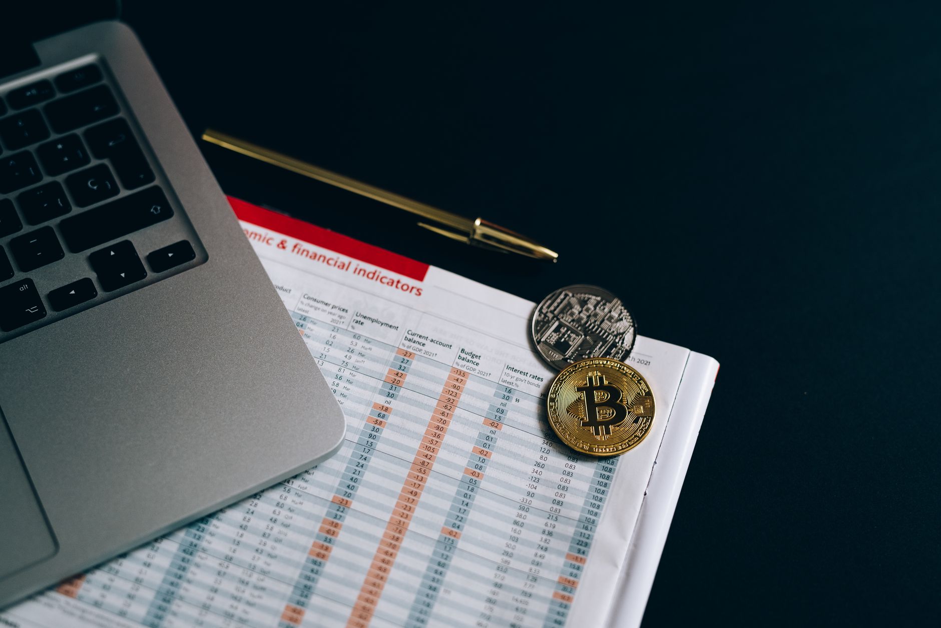 Bitcoin and cryptocurrency coins placed on a financial document next to a laptop.