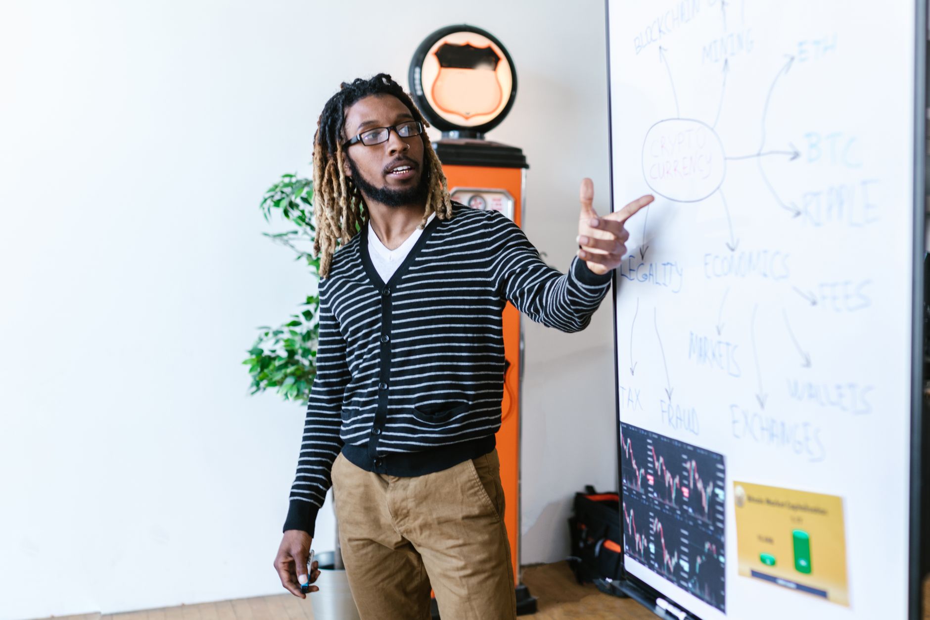 Man explaining cryptocurrency concepts on a whiteboard in a modern office setting.