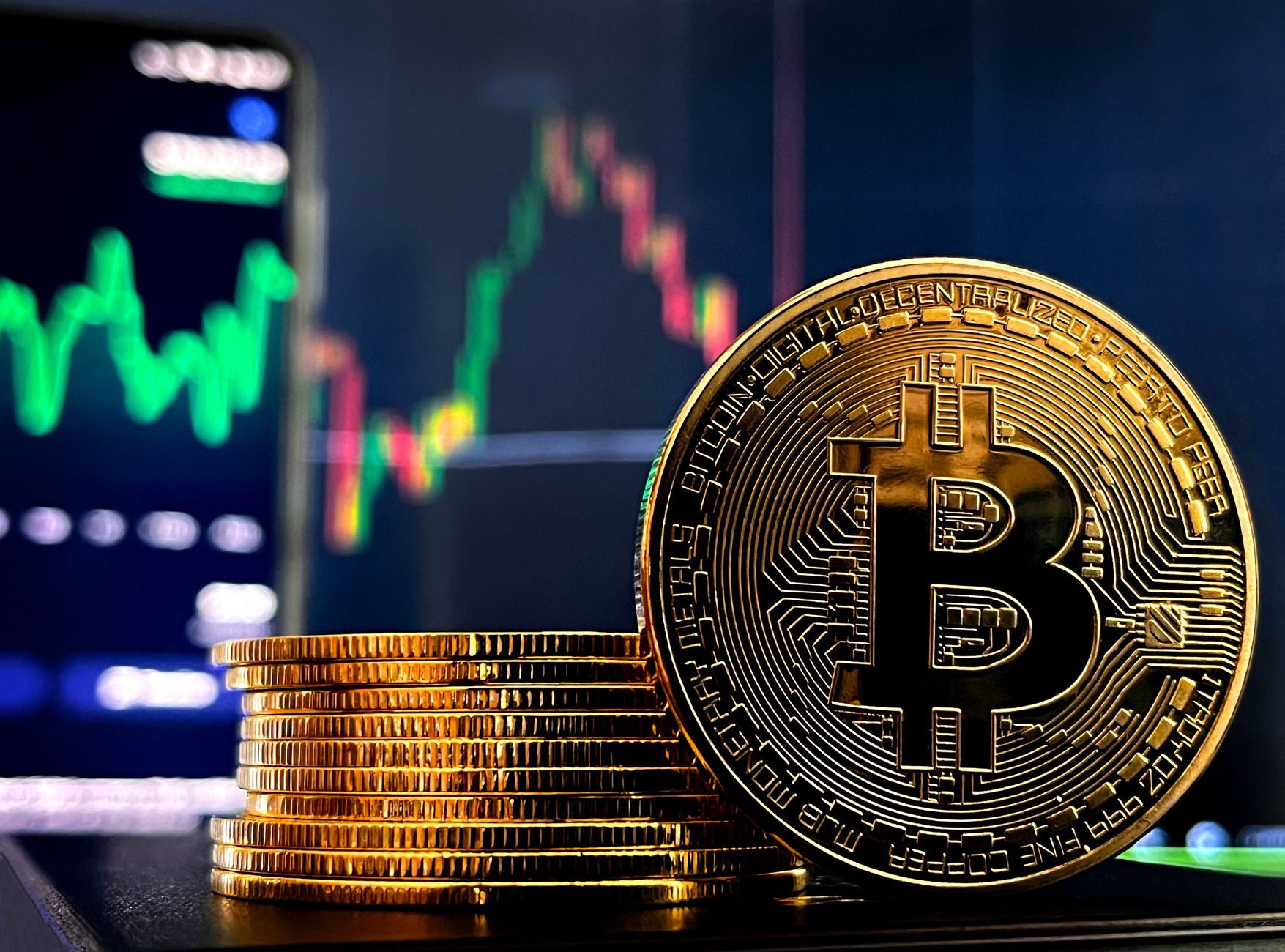 Stack of Bitcoin coins in front of a colorful stock market graph display.