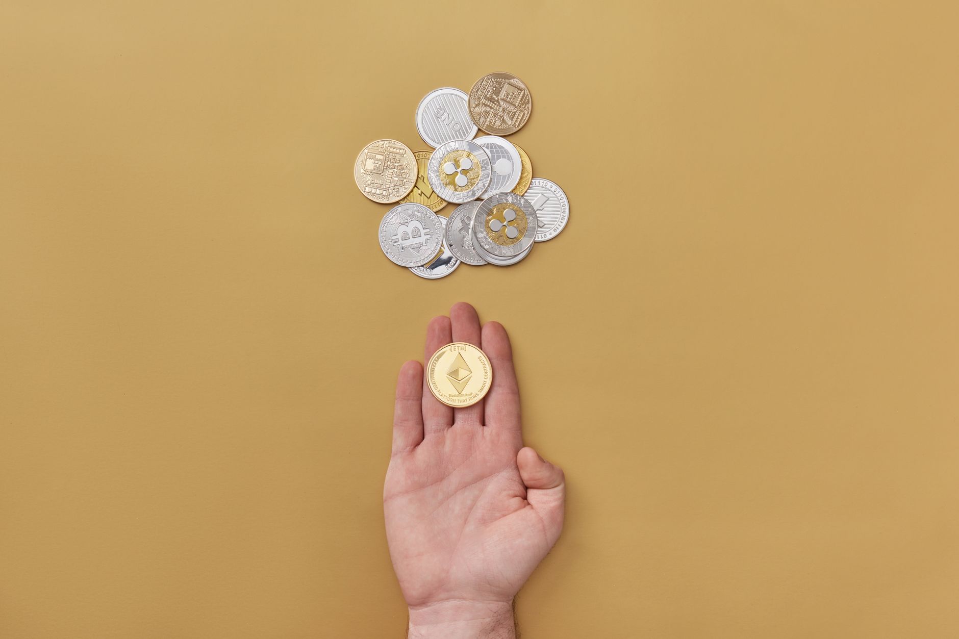 Close-up of a hand holding a cryptocurrency coin on a yellow background with scattered coins.