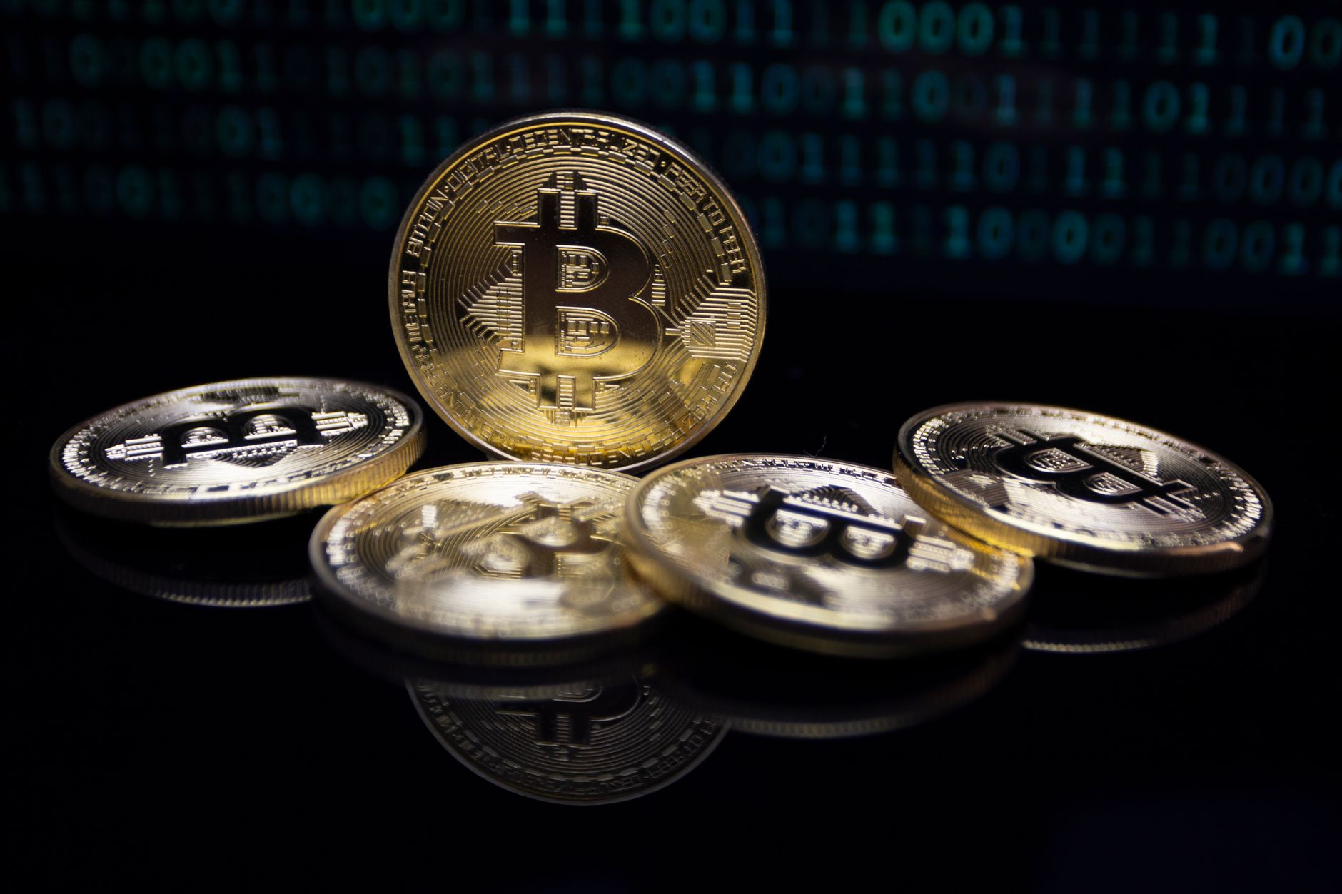 Close-up of gold Bitcoin coins against a digital binary code background, symbolizing modern finance.