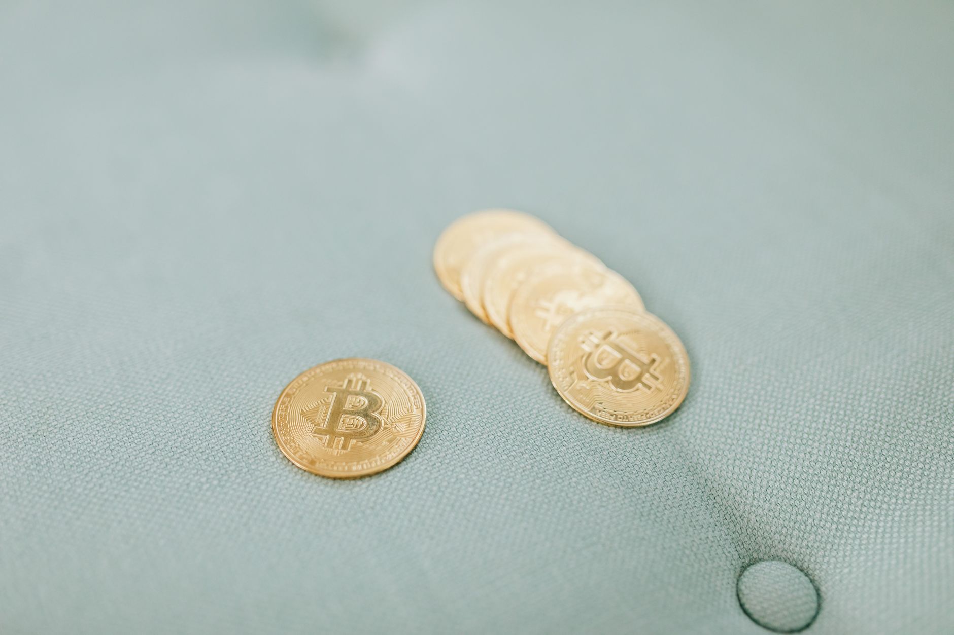 Close-up of gold Bitcoins laid on a soft blue fabric background, representing cryptocurrency wealth.